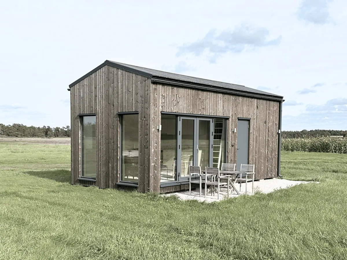 Burgsvik 30 en sommardag, med glasade pardörrar på långsidan och bord och stolar på grusplanen framför