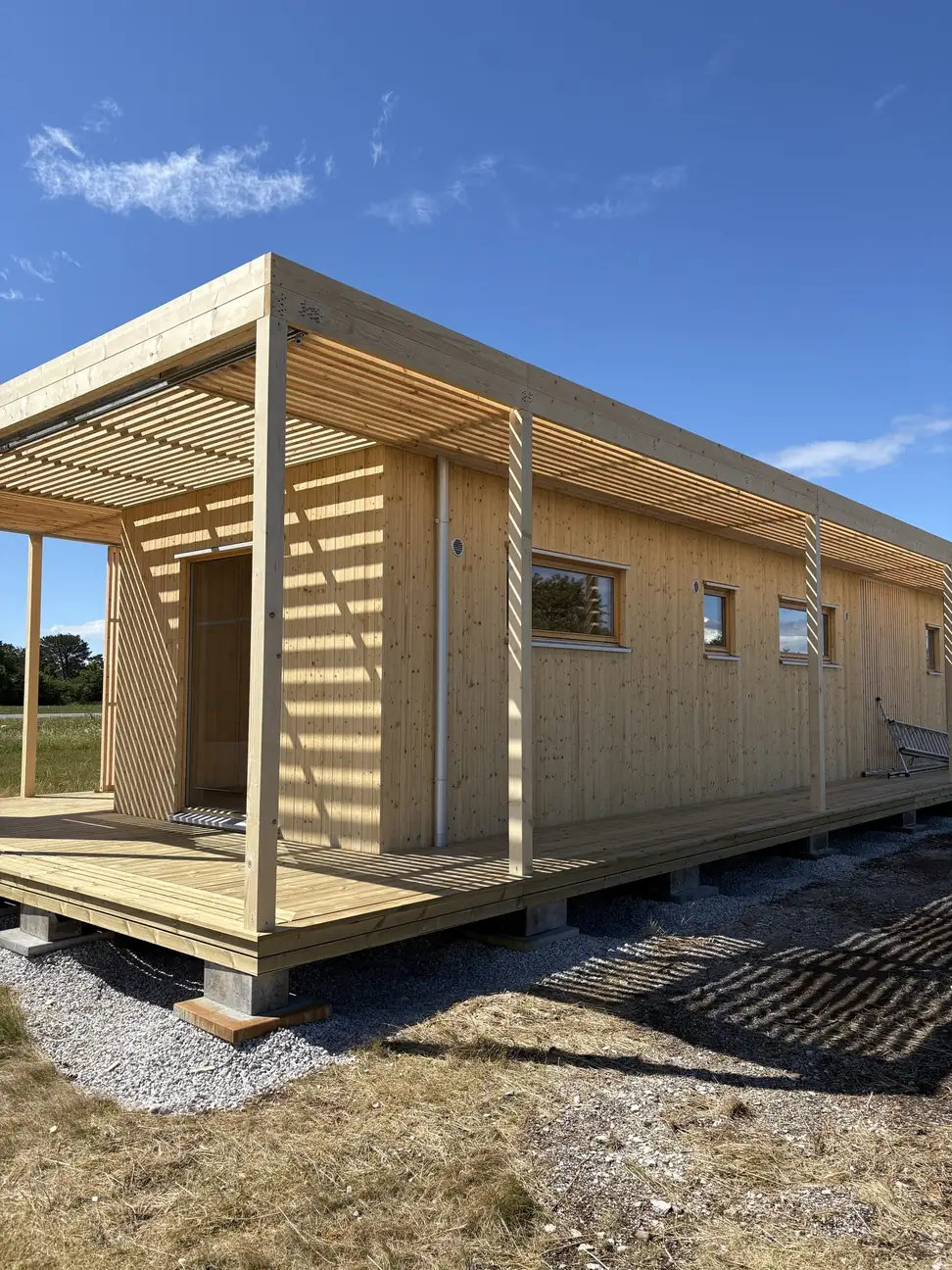Långsidan på visningshuset i Visby med entrédörr, fönster och altanen under pergolan